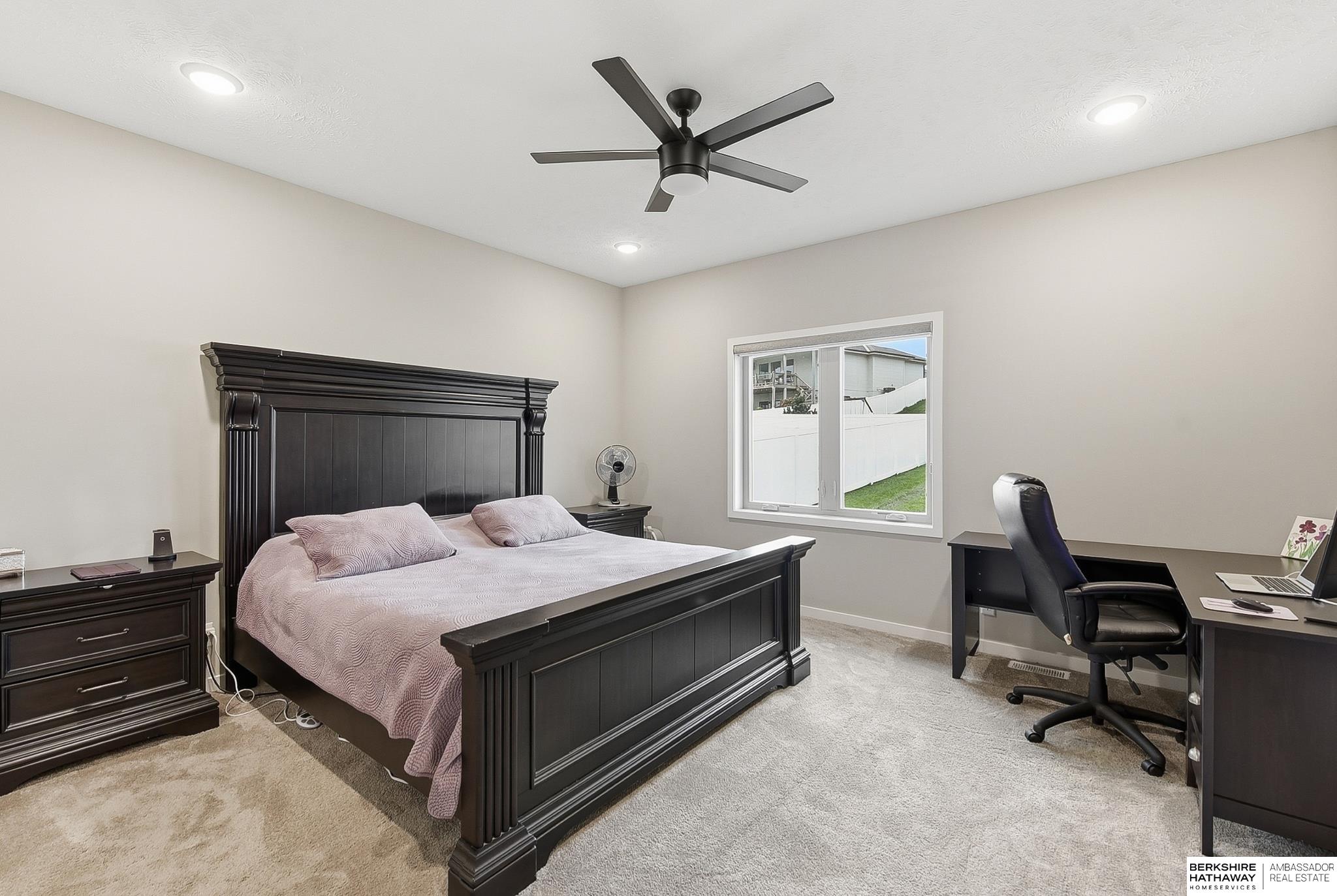 Furnished bedroom with a dark wood bed, ceiling fan, and desk beside the window.