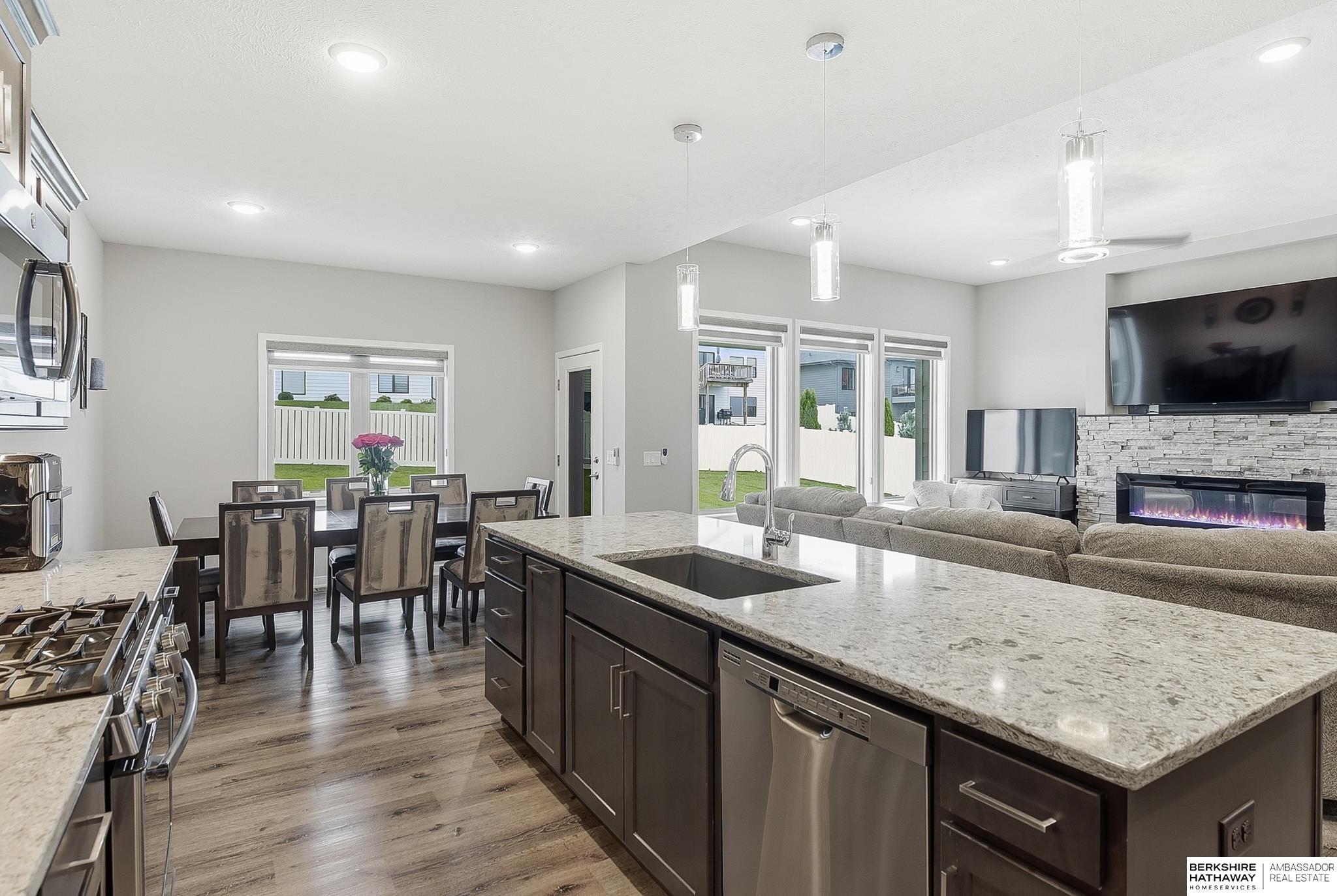Open-plan kitchen with a large granite island overlooking the dining area and living room with a stone fireplace.