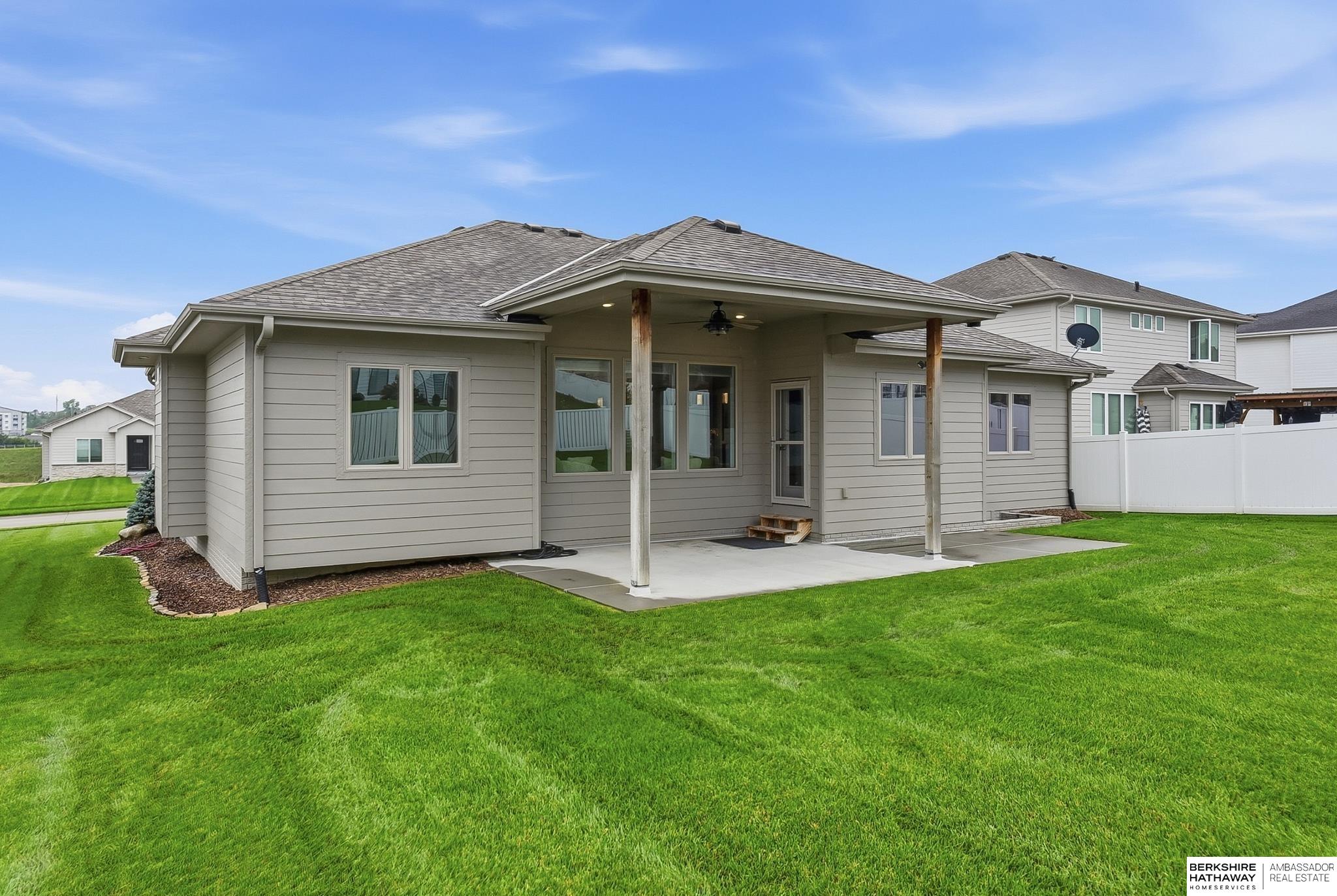 Home’s gray rear exterior with a covered patio and broad green lawn.