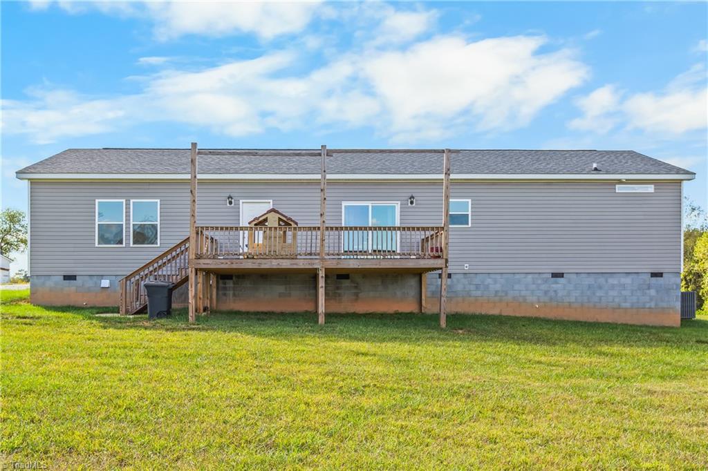 Rear of a gray-sided home with a raised wooden deck and broad grassy yard.