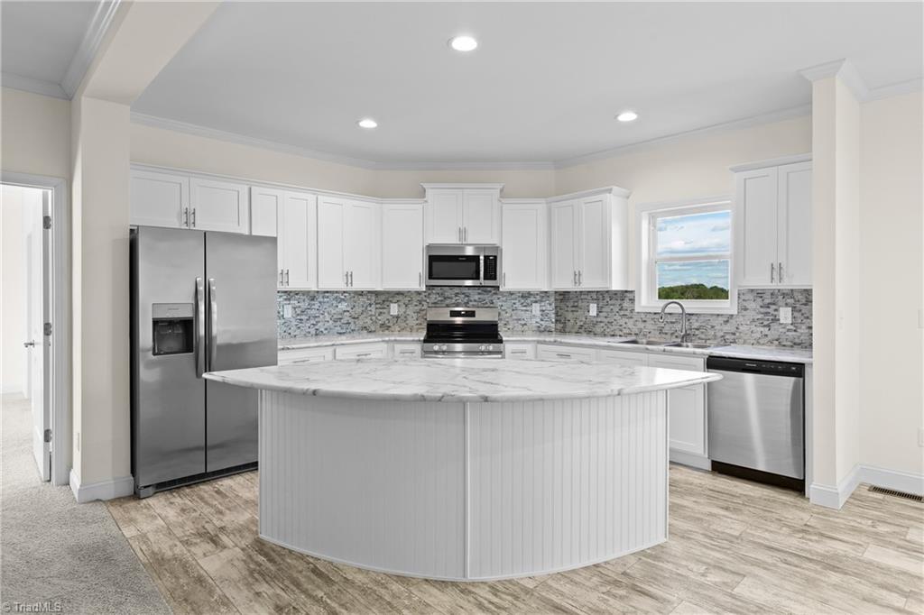 White kitchen with a large marble-look island, stainless steel appliances, and gray mosaic backsplash.