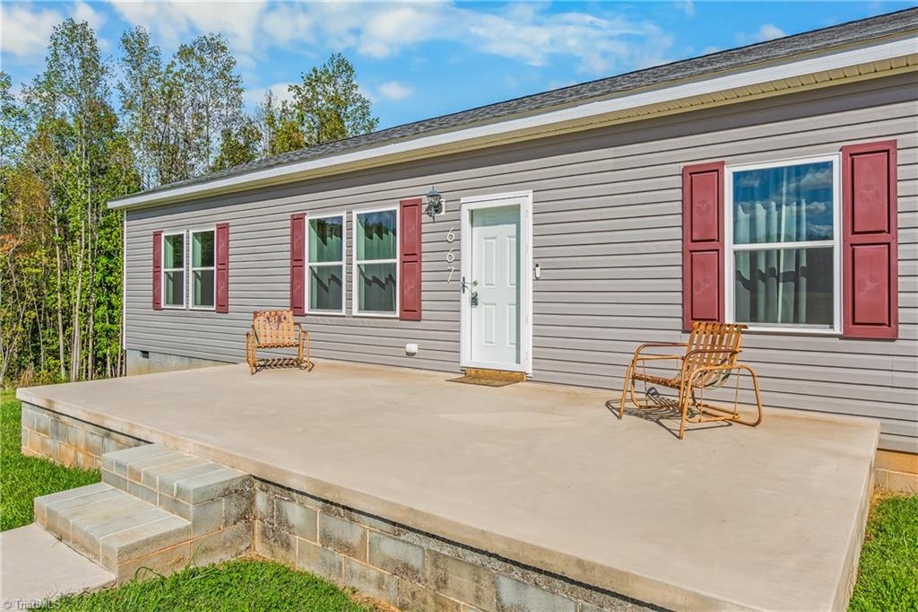 Single-story gray home with red shutters and a raised concrete patio with two chairs.