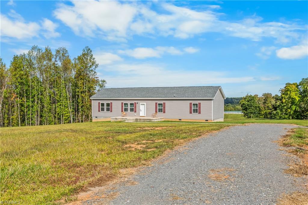 Single-story home with red shutters beside a gravel driveway and open grassy yard.