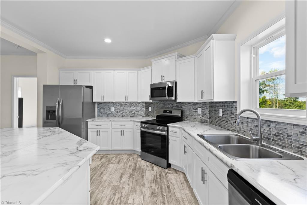Modern white kitchen with a marble-look island, gray tile backsplash, and double-basin sink by a window.