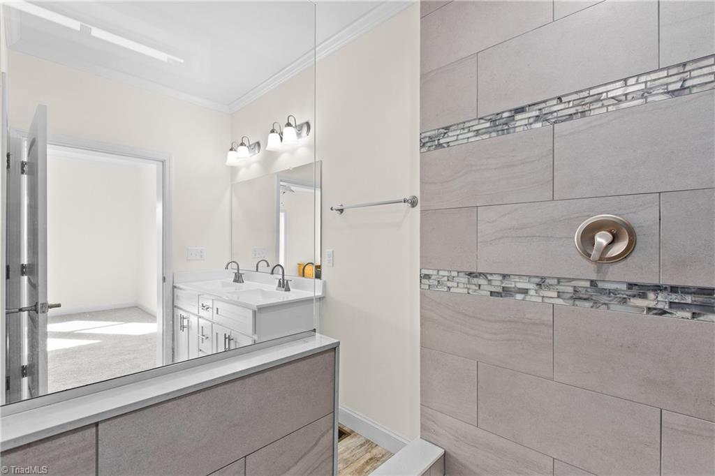Bathroom with a tiled shower, decorative mosaic bands, and a white double-sink vanity.