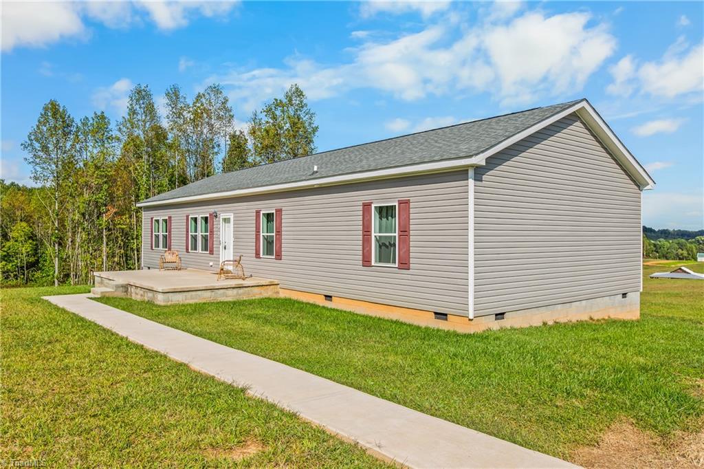 Single-story gray-sided home with red shutters, a concrete patio, and a walkway across the lawn.
