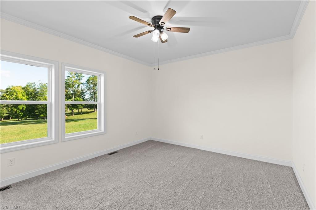 Vacant bedroom with gray carpet, two lawn-facing windows, and a ceiling fan.