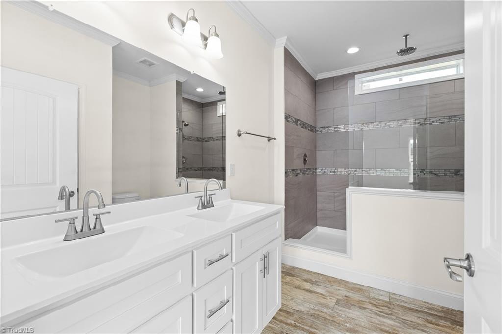 Bathroom with a double-sink vanity and glass-enclosed gray tiled shower.