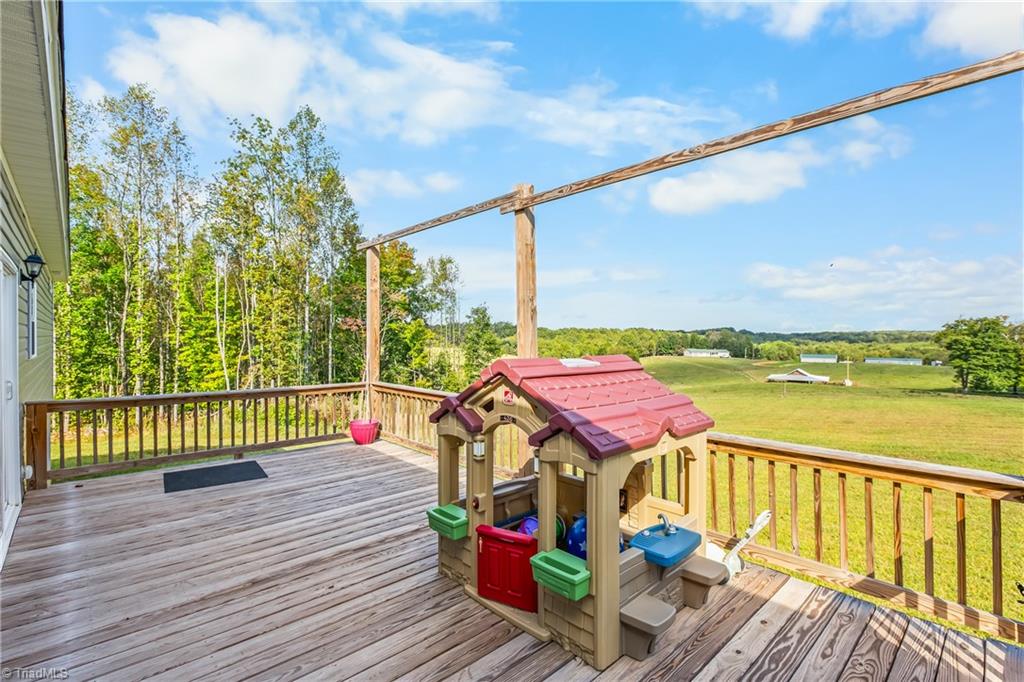 Wooden deck with a children's playset overlooking open fields and woods.