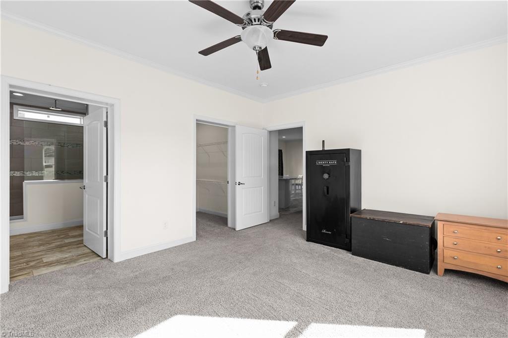 Carpeted bedroom with a ceiling fan, open closet and bathroom doors, and a large black safe.