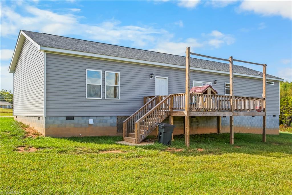 Gray single-story home with a raised wooden deck and stairs beside a grassy yard.