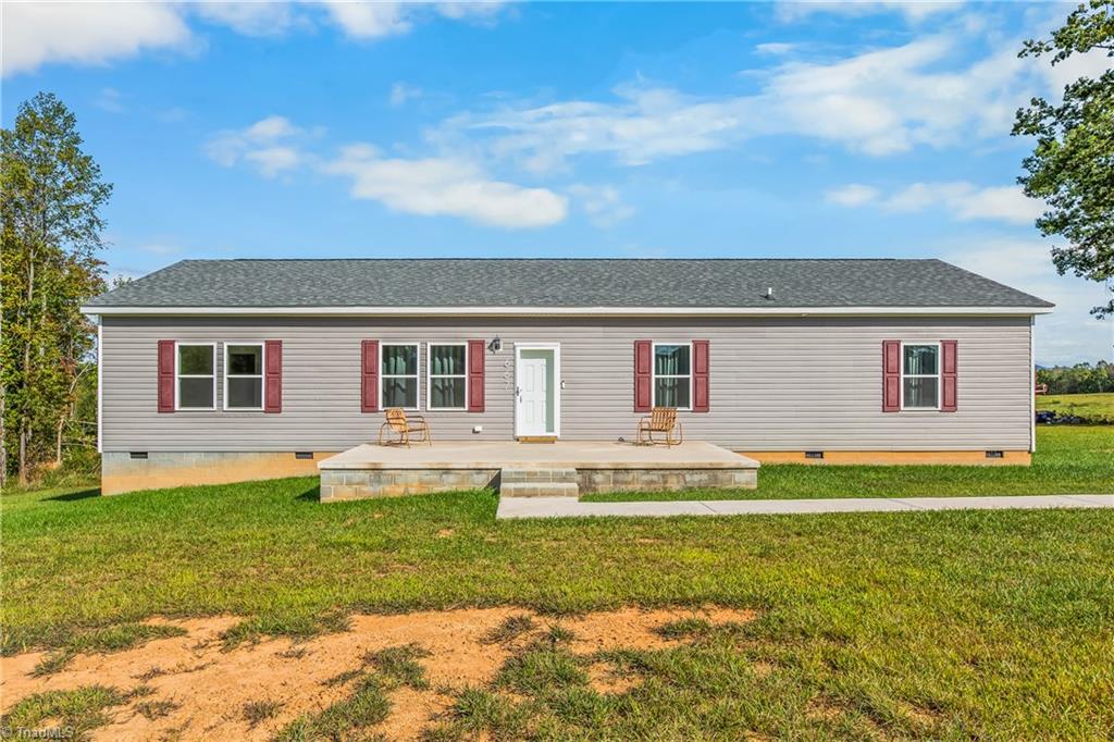 Single-story gray home with red shutters, a raised patio, and a broad green lawn.