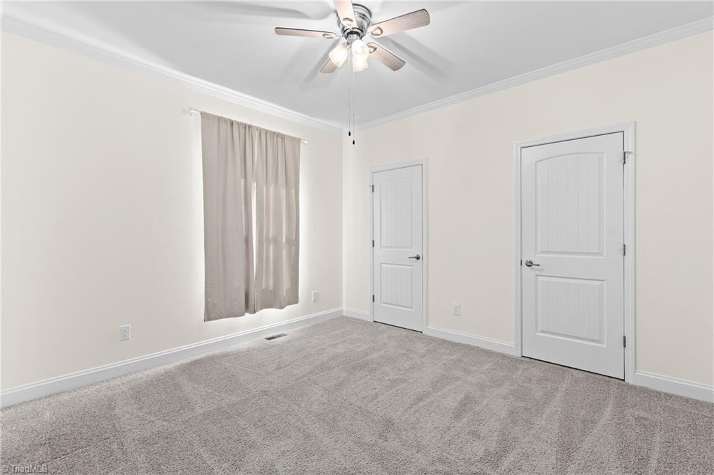 Empty bedroom with gray carpet, a curtained window, two doors, and a ceiling fan.