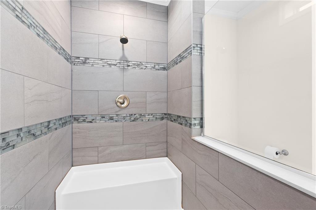 Bathroom bathtub with gray tiled shower surround and decorative mosaic bands.