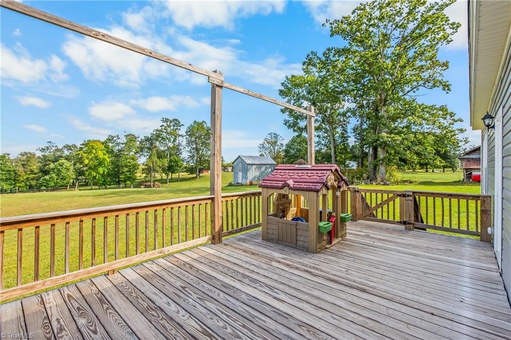 Wooden deck with a children's play structure overlooking a grassy yard and blue shed.