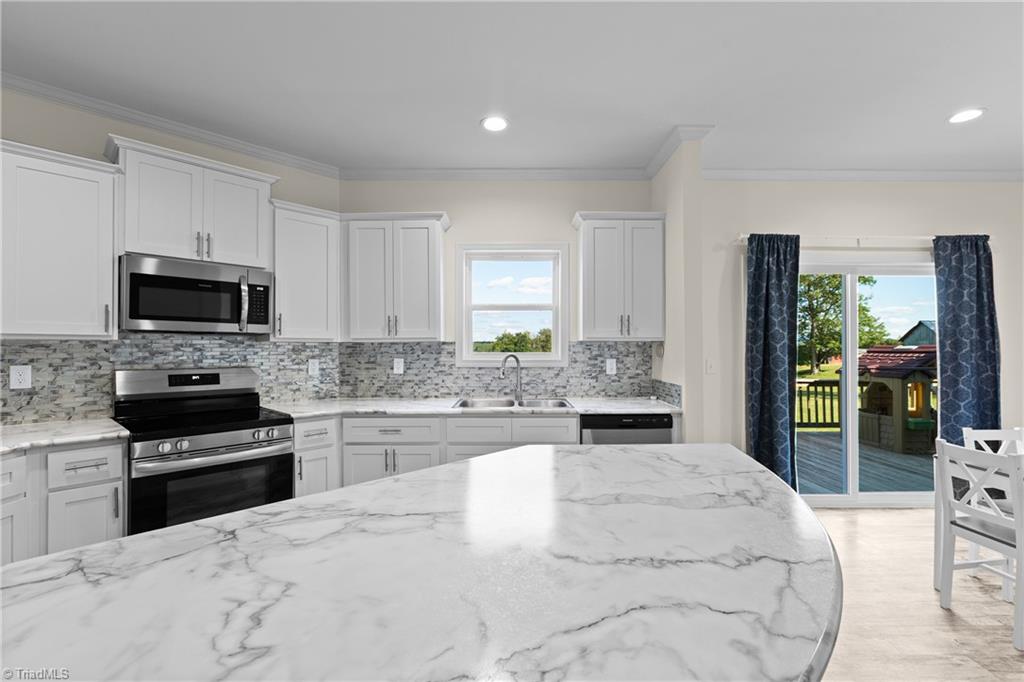 Bright white kitchen with a marble-look island, stainless appliances, and sliding doors opening onto a deck.