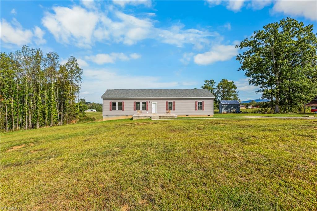 Gray ranch house with red shutters and a front porch beyond a broad lawn.