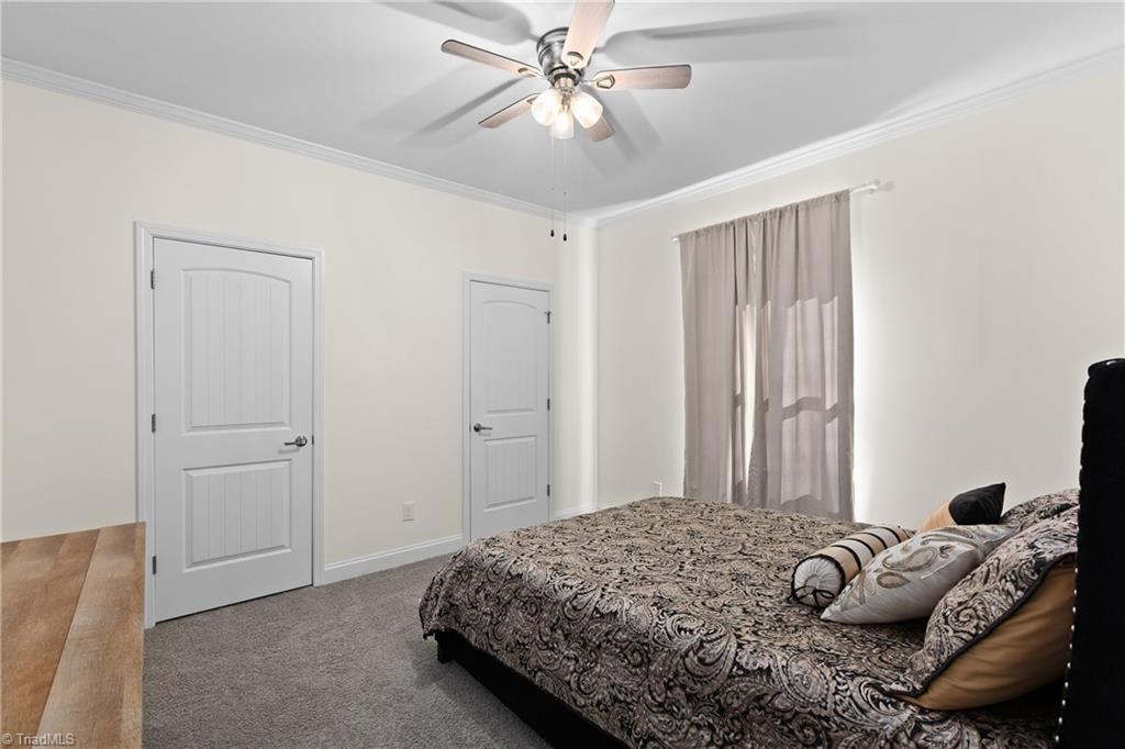 Furnished bedroom with a patterned bed, gray carpet, ceiling fan, and curtained window.
