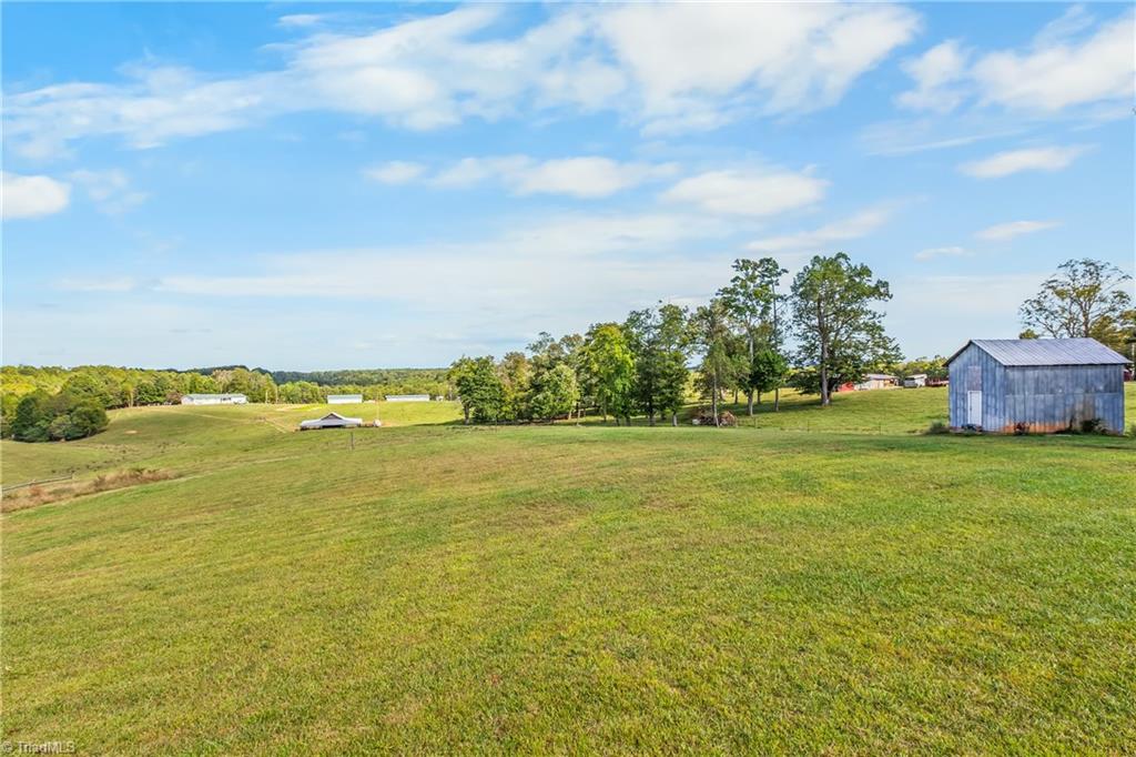 Rolling grassy acreage with scattered trees, distant farm buildings, and a small blue shed.