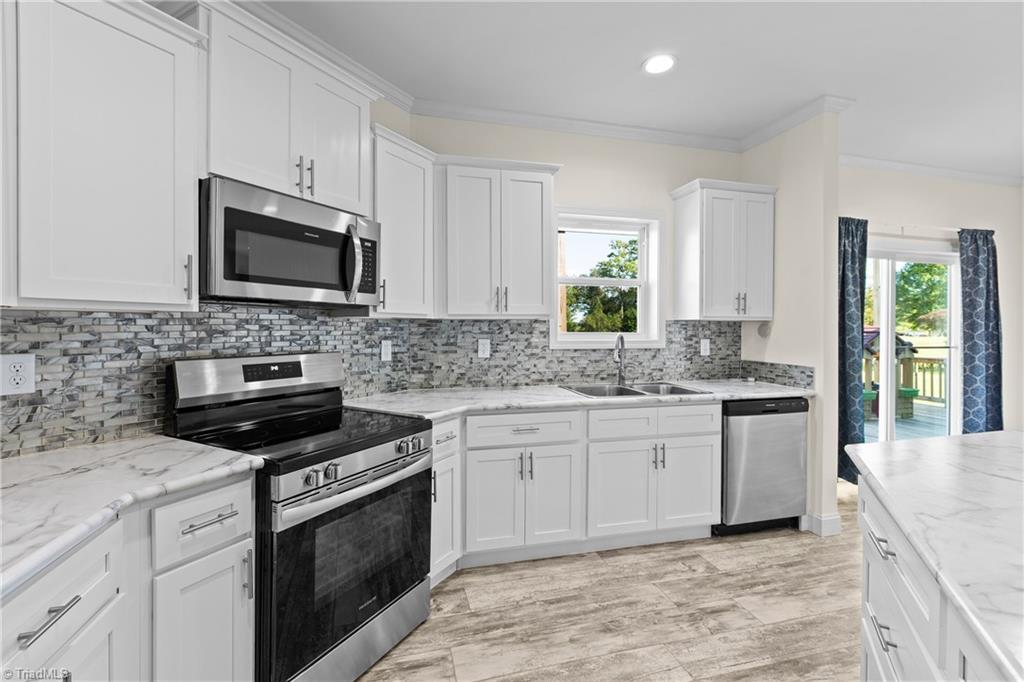 Kitchen with white shaker cabinets, gray mosaic backsplash, stainless steel appliances, and a window above the sink.
