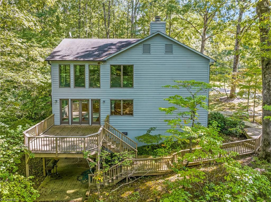 Rear of a blue-gray two-story house with a raised deck surrounded by mature trees.