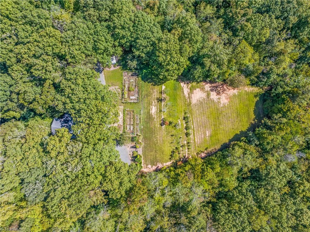 Aerial view of a wooded property with a grassy clearing and rows of garden beds.
