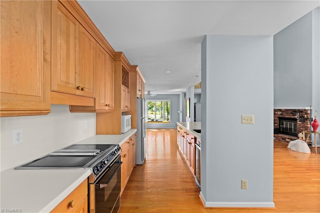 Kitchen with honey-colored cabinets and a stainless steel range opening onto a sunlit living area.