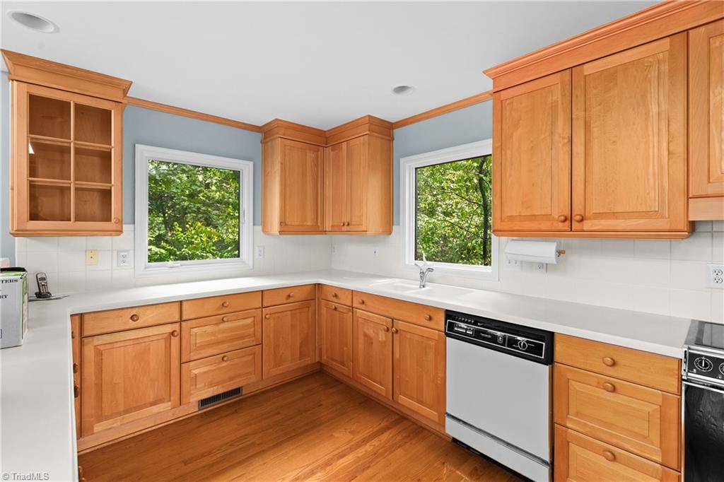 Kitchen with warm wood cabinets, white countertops, hardwood floors, and two windows overlooking greenery.