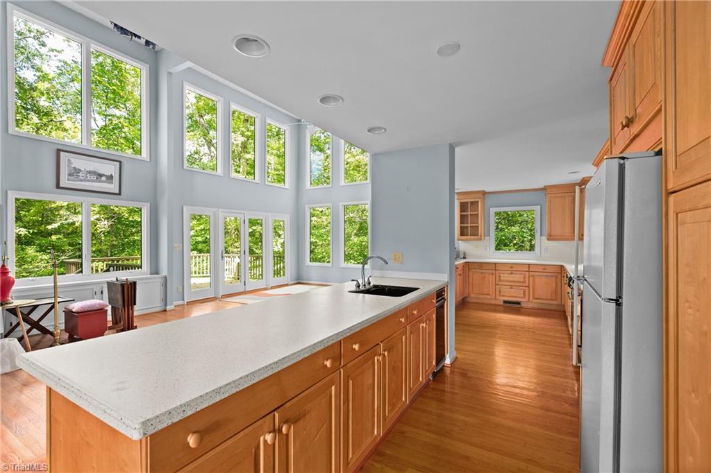 Kitchen with a long white island, honey-toned cabinets, and tall windows overlooking trees.