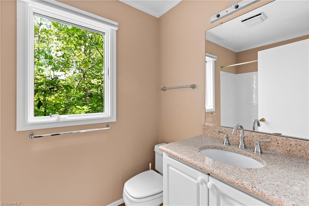 Bathroom with a stone vanity and large window overlooking leafy trees.
