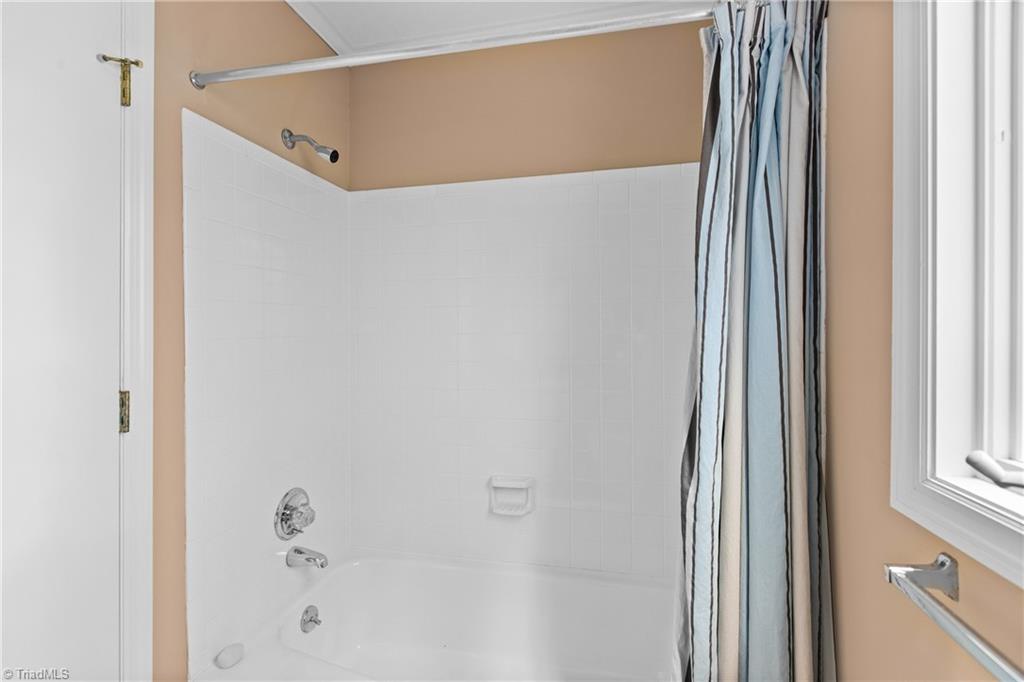 Bathroom tub and shower with white tile, chrome fixtures, and a blue-and-white striped curtain.