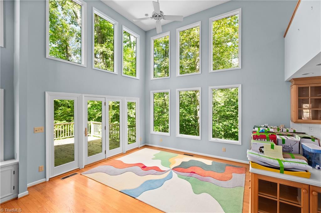 Two-story living room with tall windows, deck doors, hardwood floors, and a colorful rug.