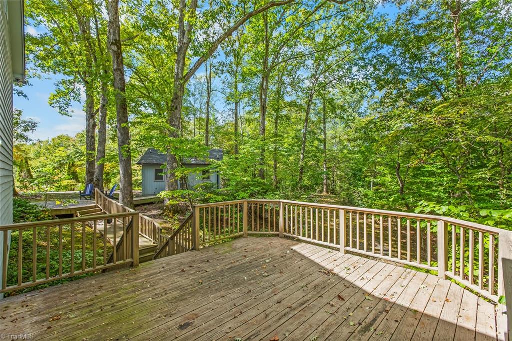Wooden deck overlooking a leafy wooded yard, with stairs and a small outbuilding.