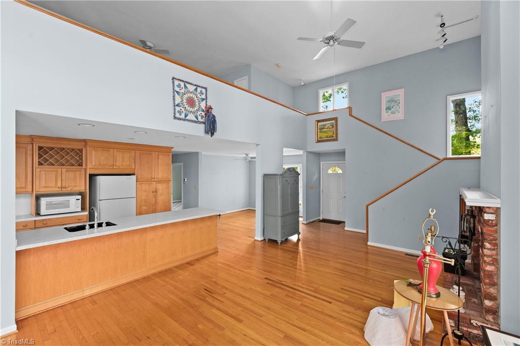 Open-plan kitchen and living area with hardwood floors, a two-story ceiling, staircase, and brick fireplace.