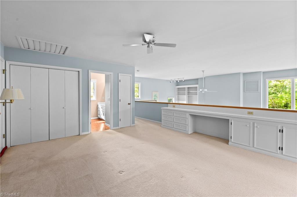 Empty carpeted room with large closets, built-in white cabinetry, and windows overlooking greenery.