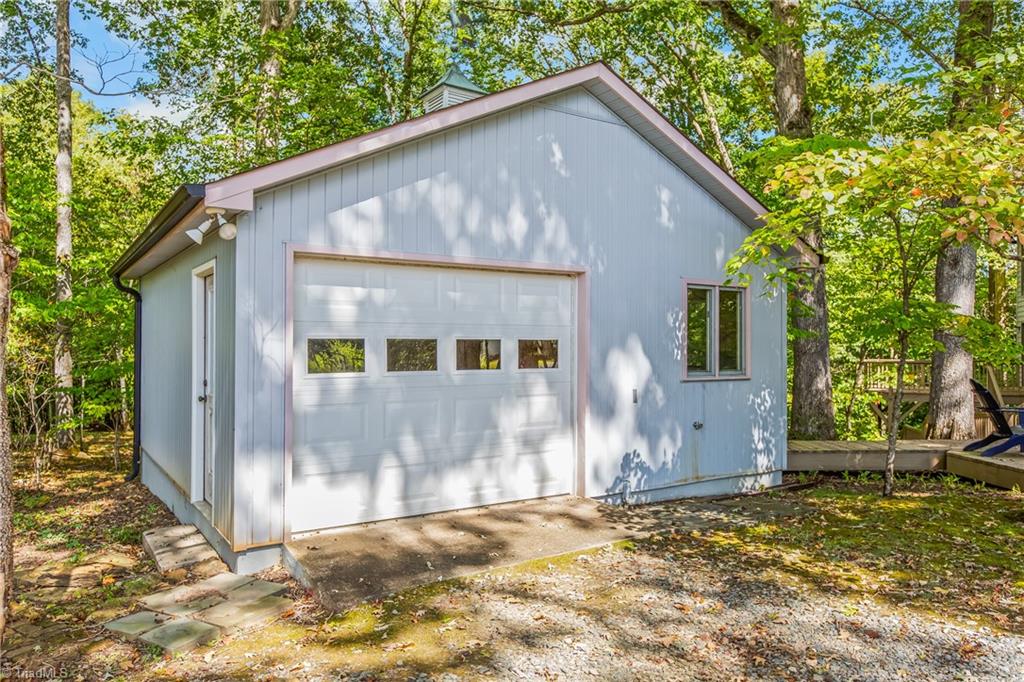 Light blue detached garage with a four-window overhead door, surrounded by leafy trees.