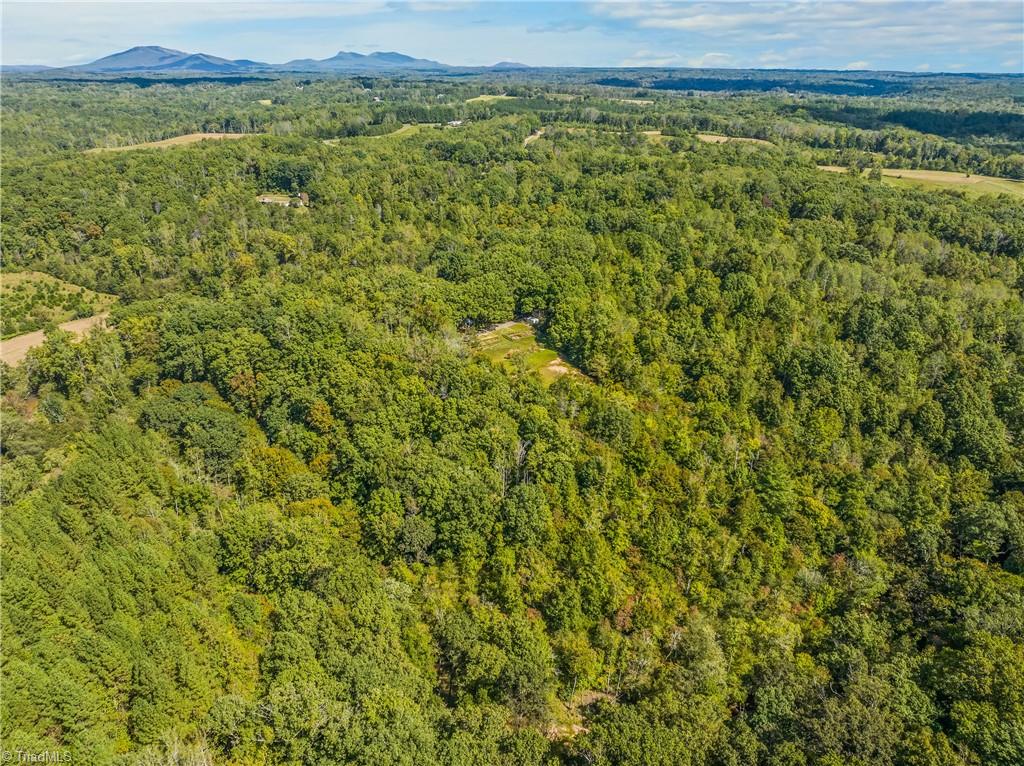 Wooded property with a small clearing and distant mountain ridges, photographed from above.