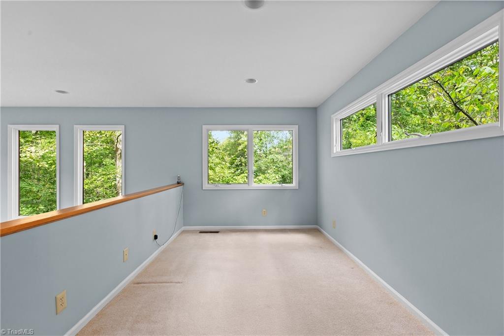 Empty carpeted room with pale blue walls, multiple windows, and leafy views.
