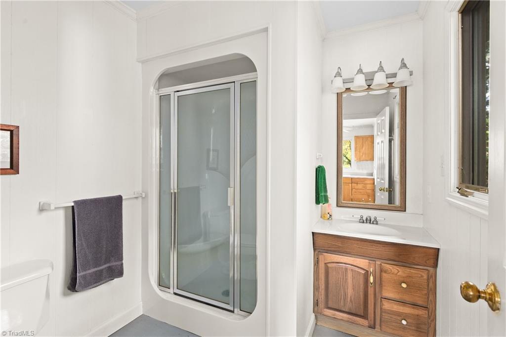 Bathroom with an arched glass shower enclosure and a wood vanity beneath a framed mirror.
