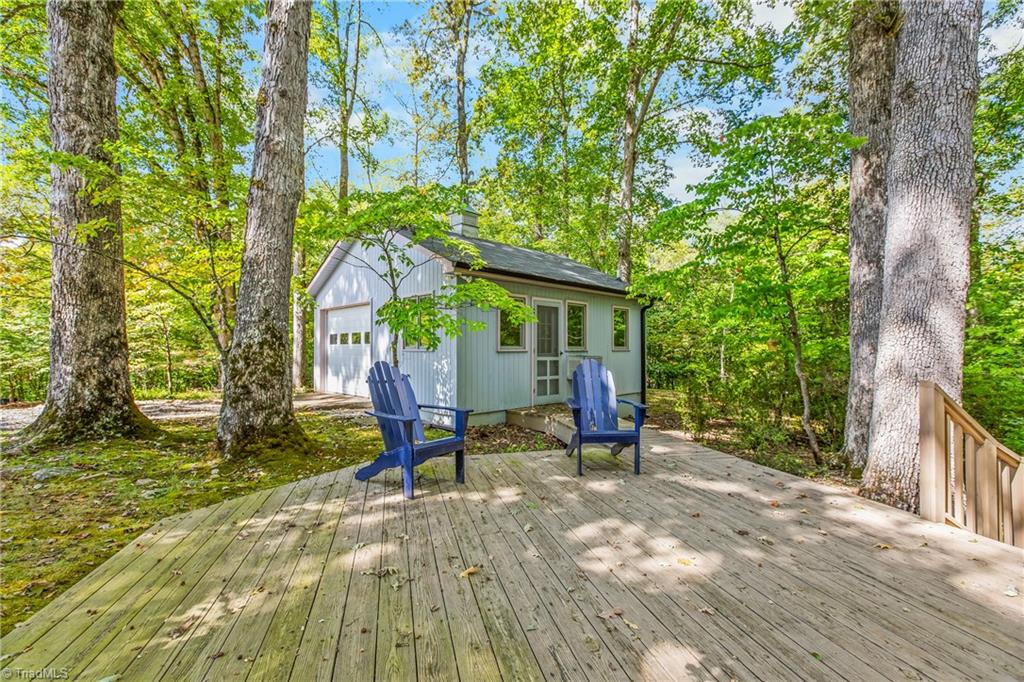 White detached building in a wooded setting, viewed from a deck with two blue Adirondack chairs.
