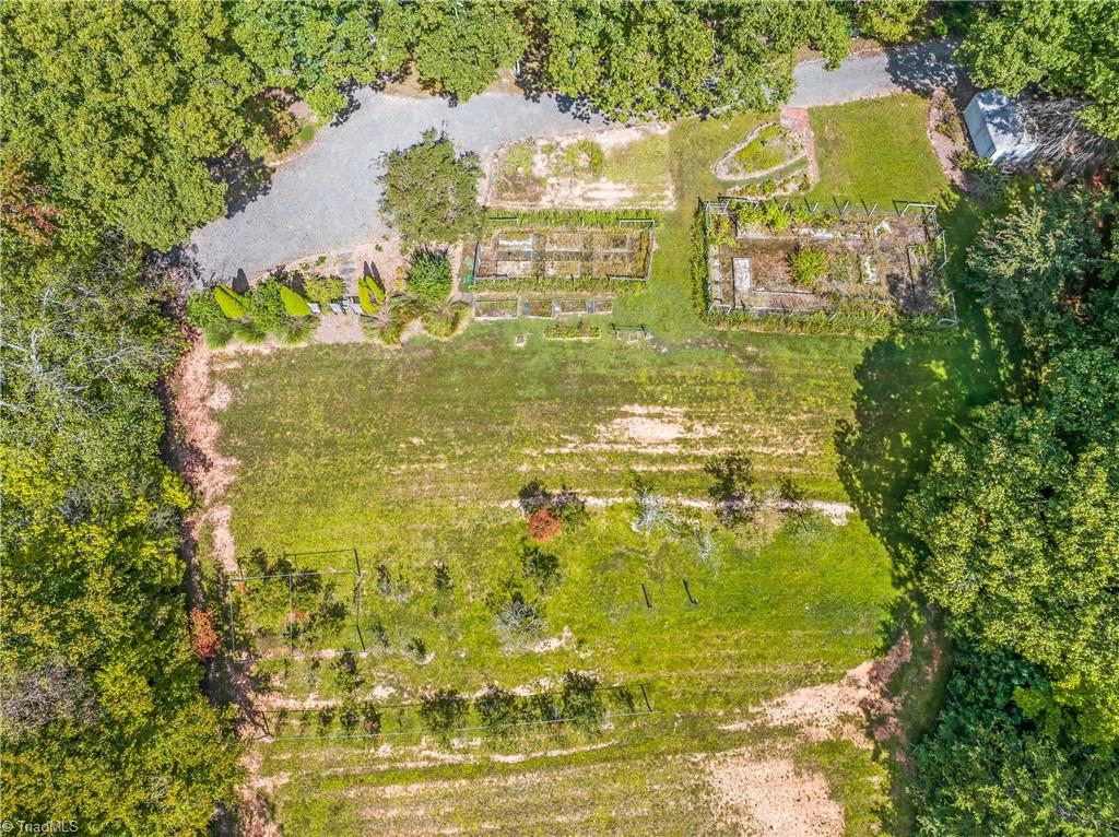 Aerial view of a wooded property with fenced garden beds and a broad grassy lawn.