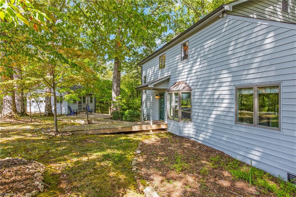 Blue-gray two-story house beside a raised deck and leafy, wooded yard.