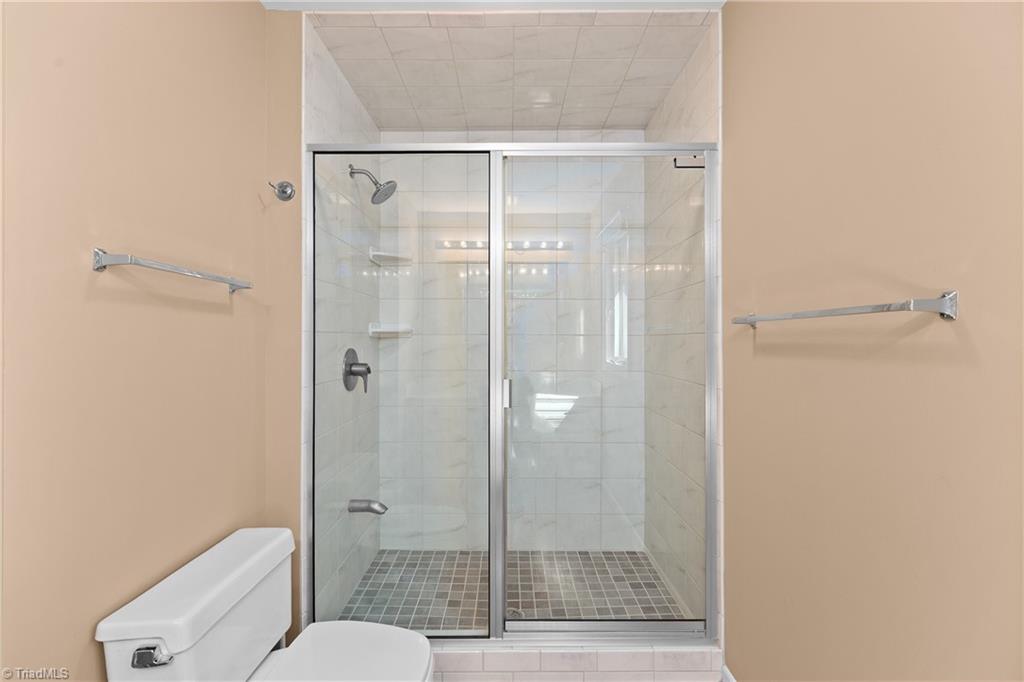 Bathroom with a glass-enclosed tiled walk-in shower and toilet in the foreground.