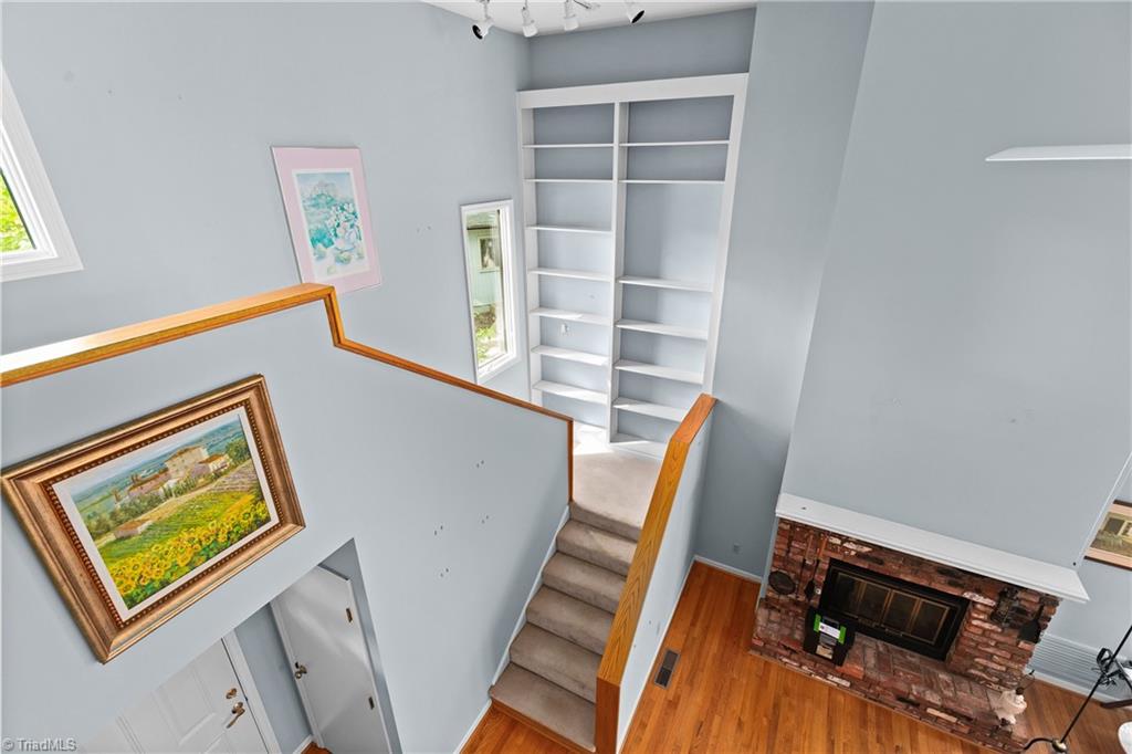 Interior staircase with built-in shelves, framed artwork, hardwood flooring, and a brick fireplace.