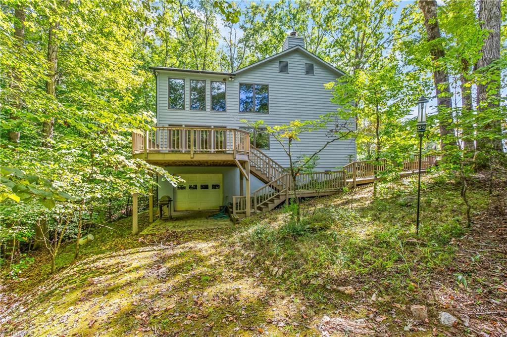 Gray two-story home with a raised deck and exterior stairs on a wooded slope.