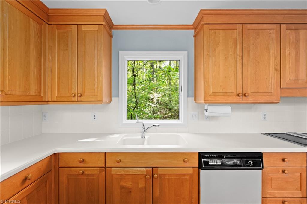 Kitchen with warm wood cabinets, white counters, and a sink beneath a window overlooking trees.