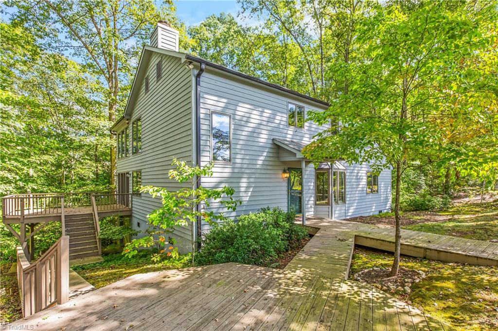 Two-story gray-sided house among trees, with a broad wooden deck and walkway to the entrance.