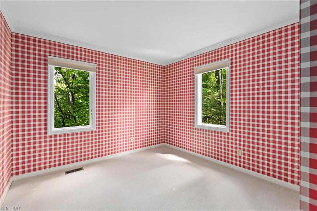 Empty room with red-and-white checkered wallpaper and two windows overlooking trees.
