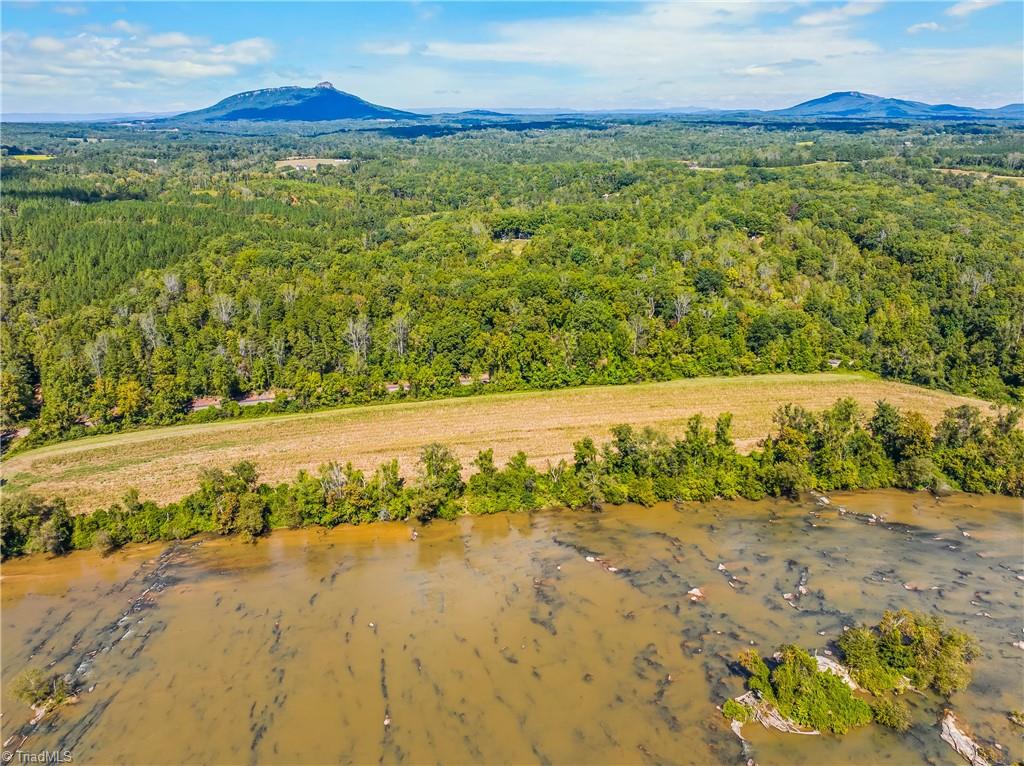 Aerial view of wooded acreage beside a shallow river, with a cleared field and distant mountain ridges.