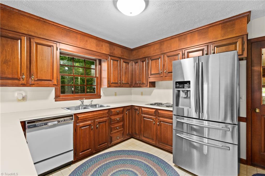 Kitchen with warm wood cabinets, white countertops, stainless steel appliances, and a window above the sink.